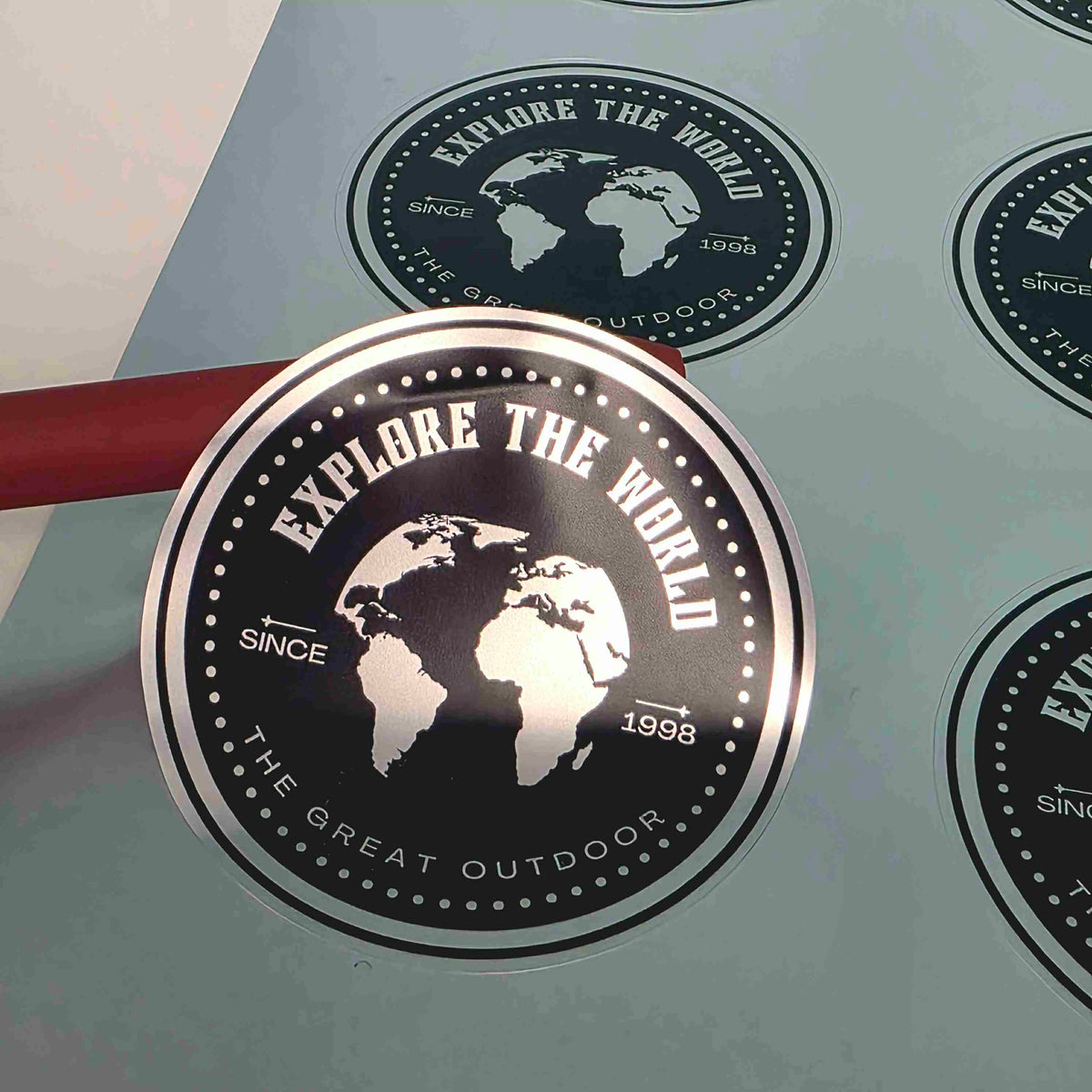 Round metallic silver vinyl sticker labels by Pure Pack, black Explore the World globe badge design on a kiss-cut sheet